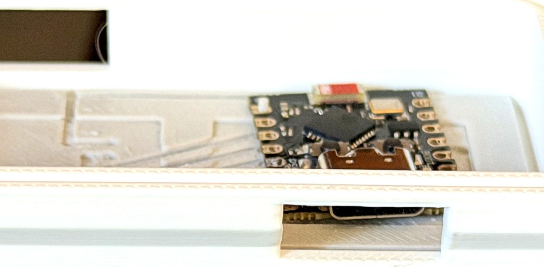 Dentro de la carcasa impresa: el ESP32-C3 asentado en su hueco mientras las trazas de cinta de cobre lijada recorren canales tallados en la base, con el USB-C alineado con la ranura impresa